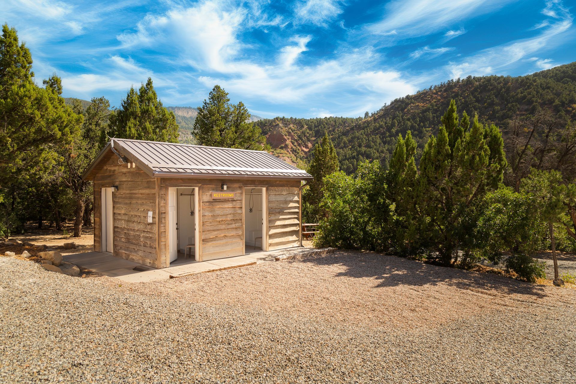 A small wooden building in the middle of a dirt field surrounded by trees.
