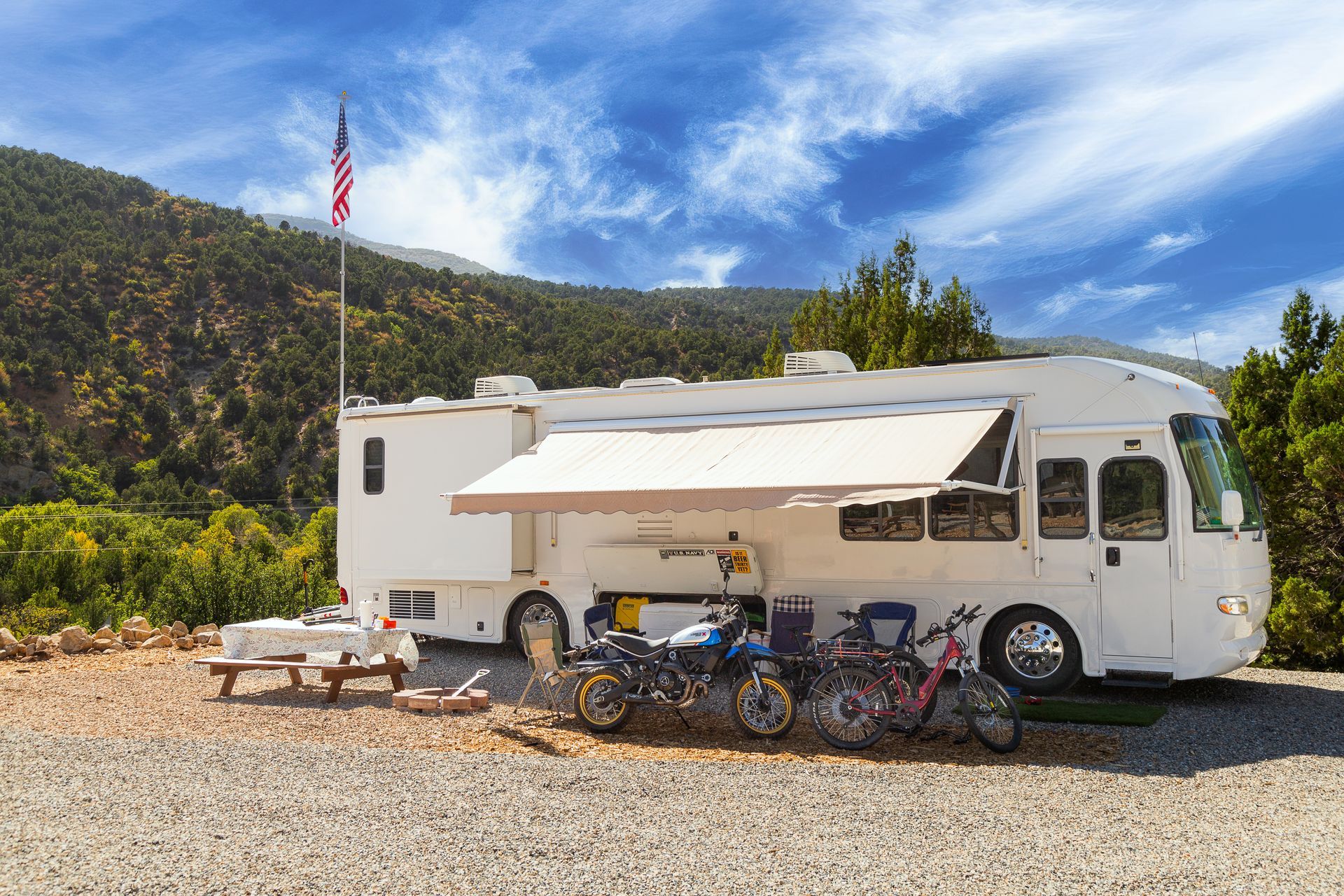 A white rv with an awning and motorcycles parked in front of it.