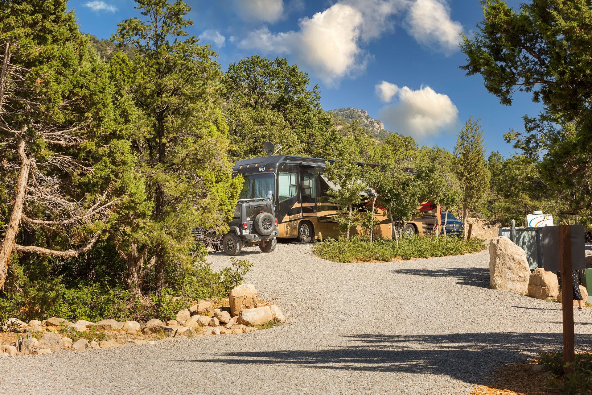 A rv is parked in a gravel lot surrounded by trees.