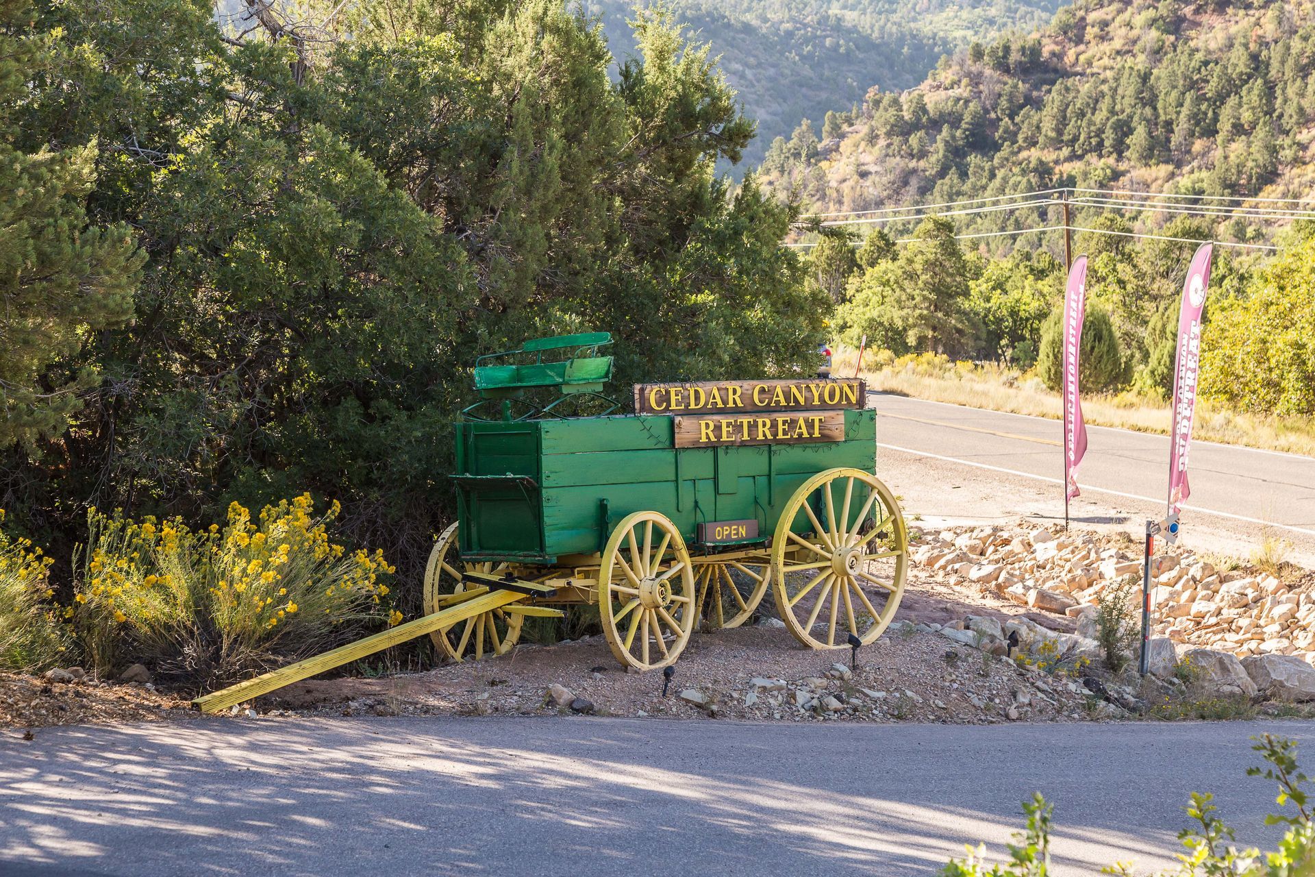 A green wagon with yellow wheels is parked on the side of the road.