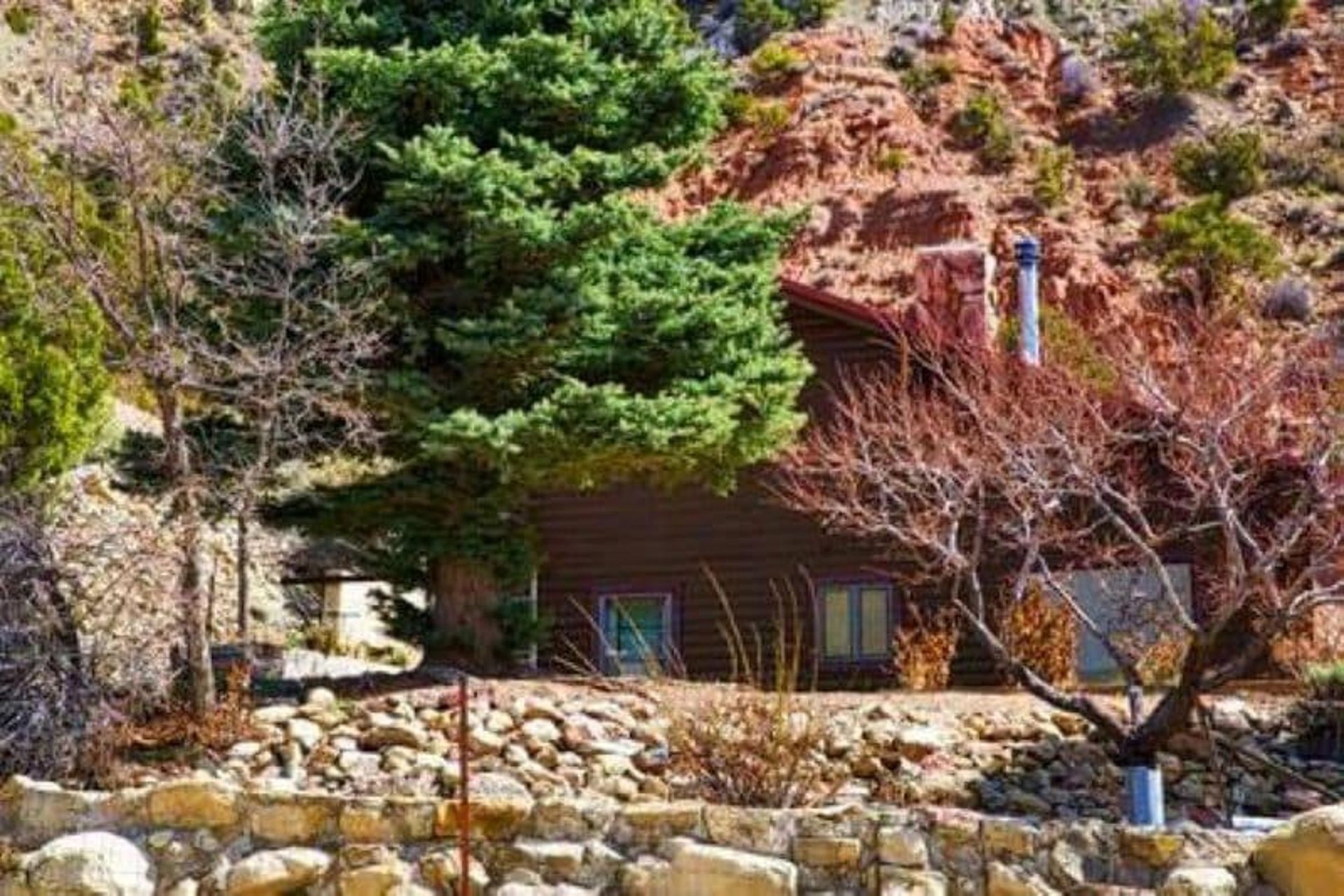 A cabin in the mountains with trees and rocks in front of it.