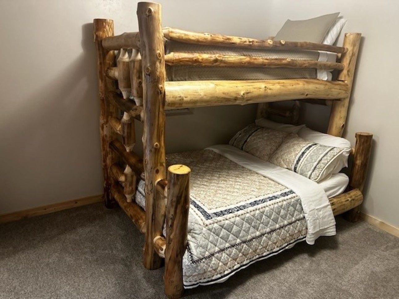A wooden bunk bed with a quilt and pillows in a bedroom.