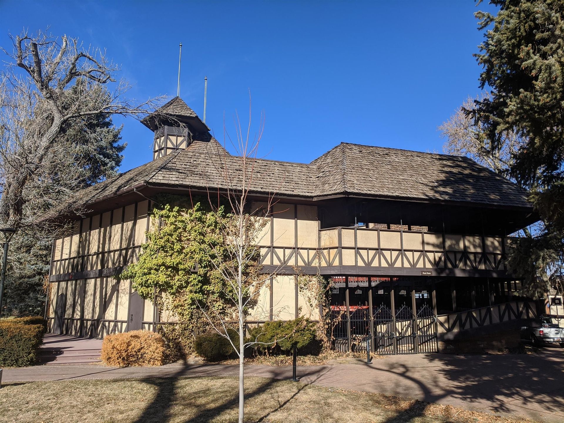 A large wooden building with a shingle roof is surrounded by trees on a sunny day.