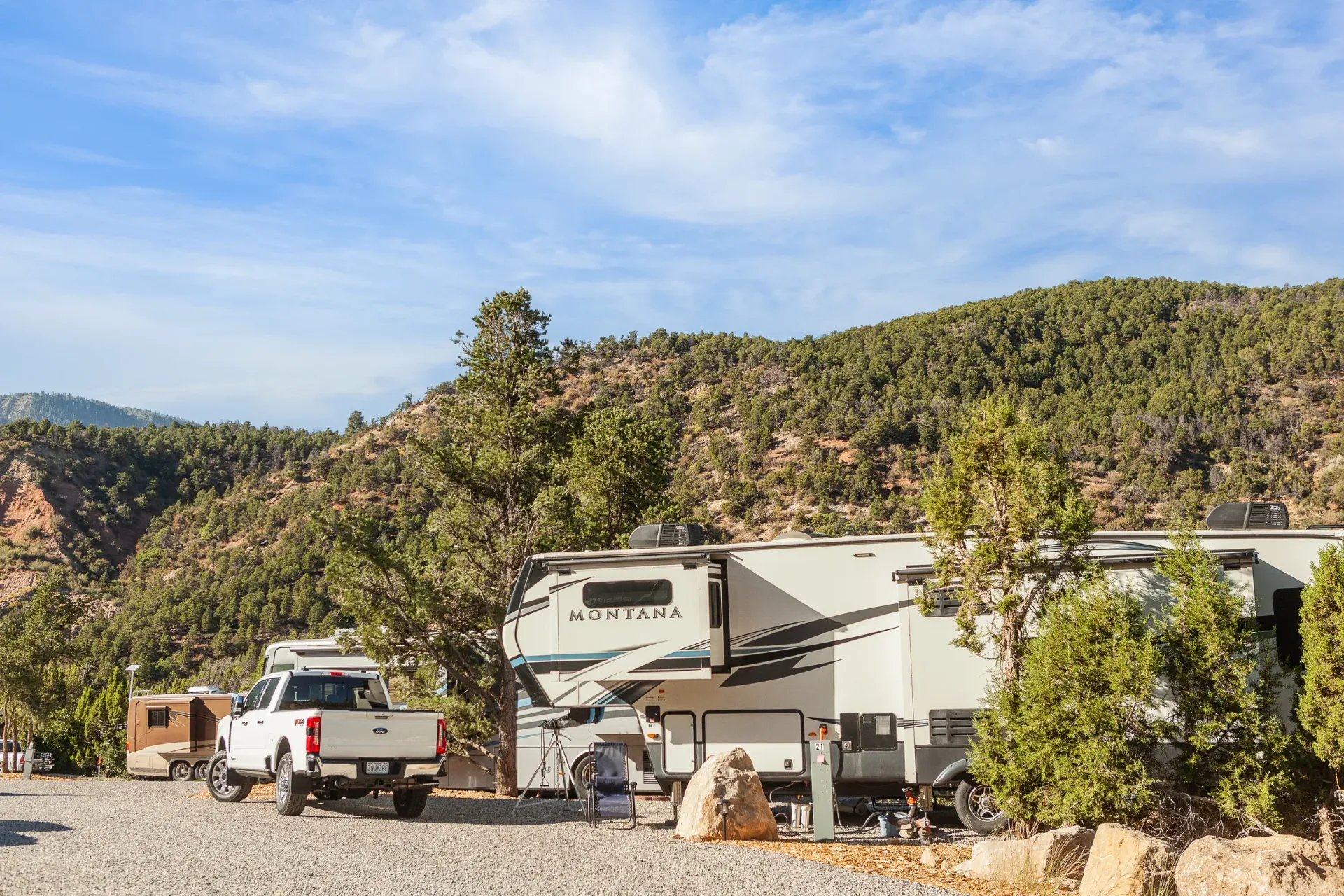 A group of rvs are parked in a gravel lot in the mountains.