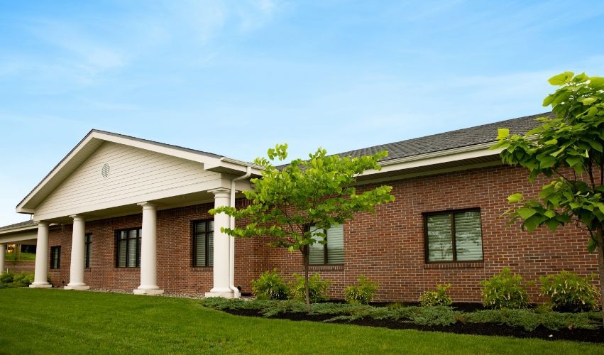 A large brick building with columns and a lush green lawn in front of it.