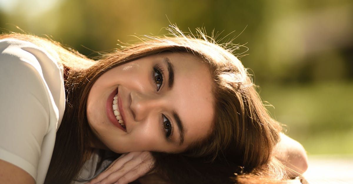 棕色頭髮的女人面帶微笑，頭靠在手上。戶外，模糊的綠色背景。