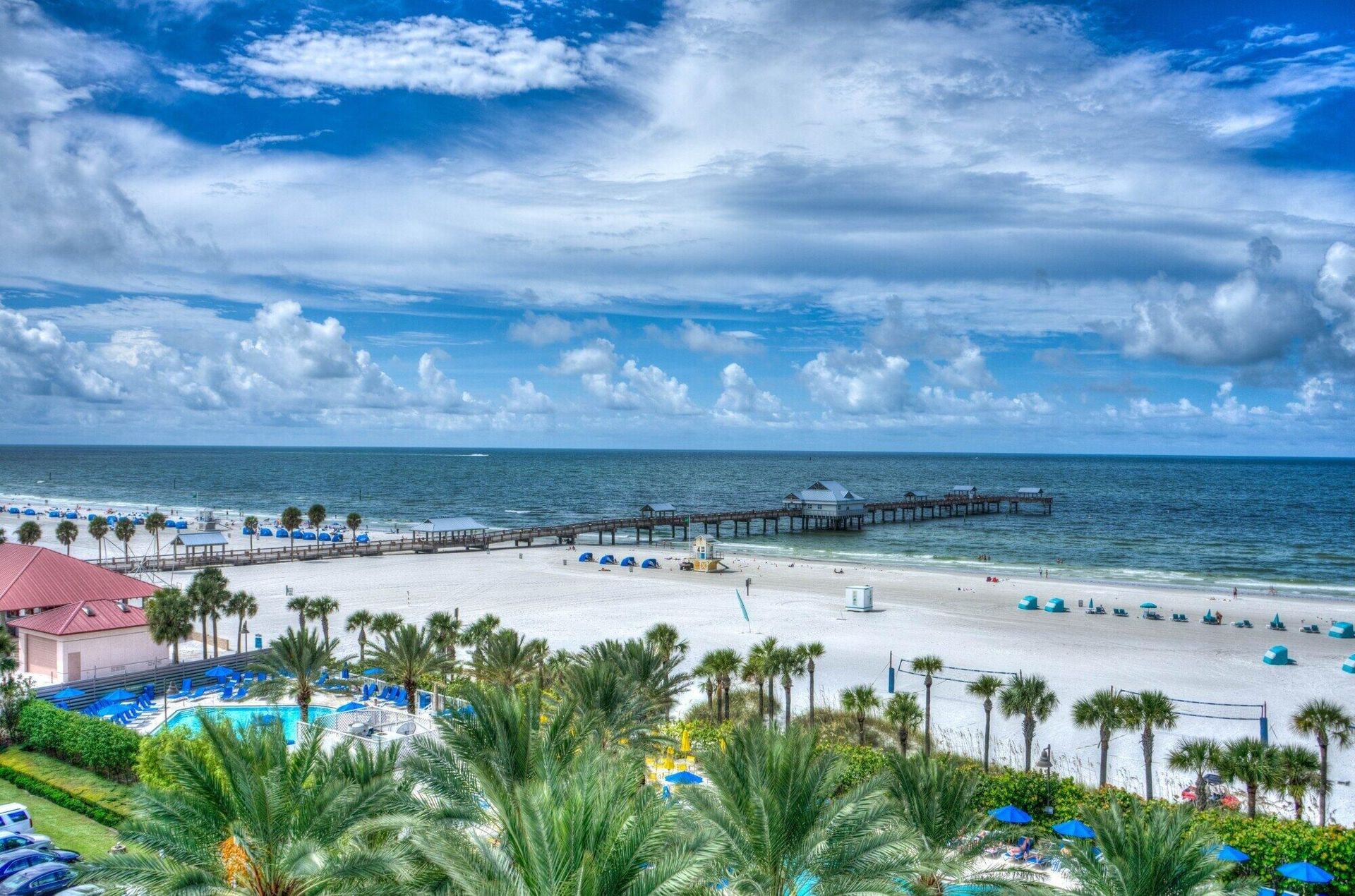 An aerial view of a beach with palm trees and a pier.