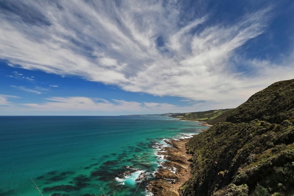 Ocean view: turquoise water, rocky shore, lush green cliffs under a bright blue sky with wispy clouds.— GMS Legal & Conveyancing In 38 Canton Beach Rd Toukley, NSW