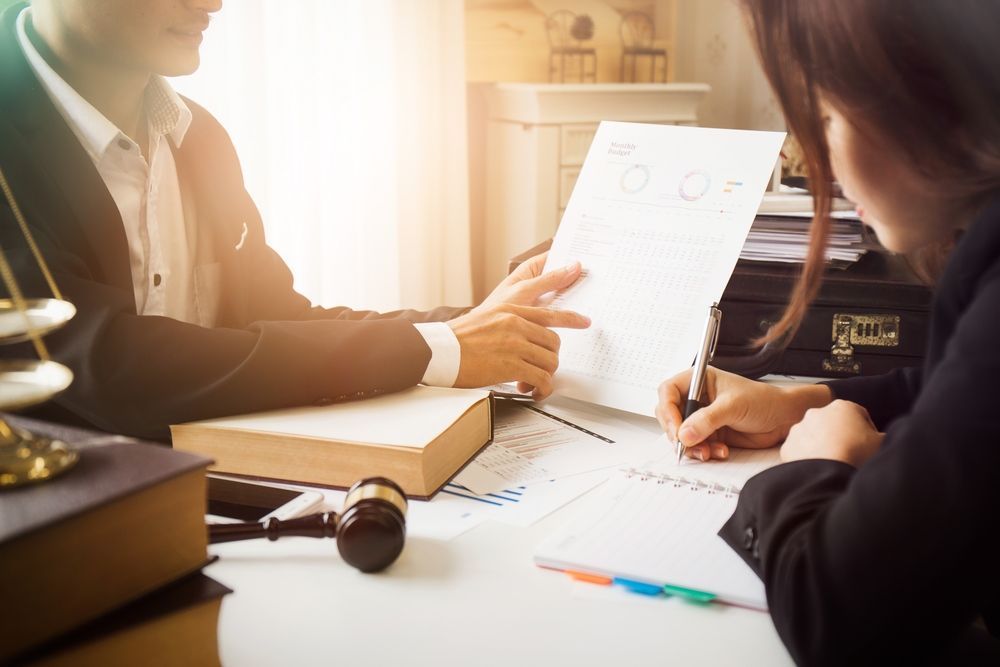 A Man And A Woman Are Sitting At A Table Looking At A Piece Of Paper — GMS Legal & Conveyancing In Hunter Valley, NSW