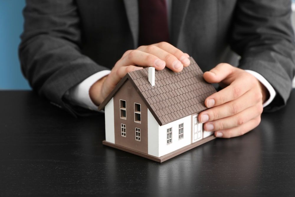 A Man In A Suit And Tie Is Holding A Model House In His Hands — GMS Legal & Conveyancing In 38 Canton Beach Rd Toukley, NSW