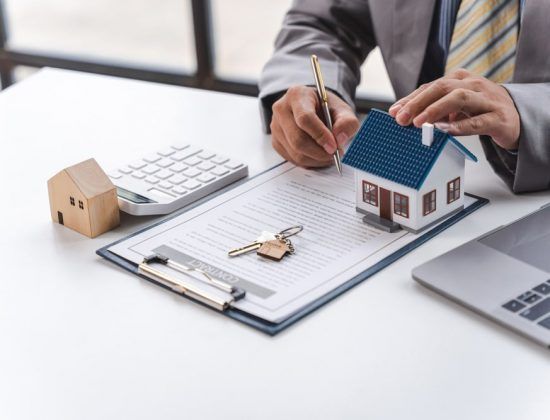 Person signing documents with toy house, keys, and calculator on a desk. GMS Legal & Conveyancing In 38 Canton Beach Rd, Toukley