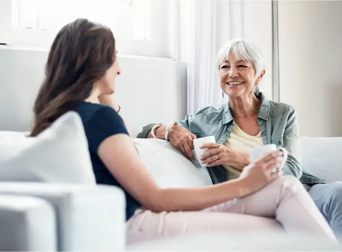 Two women sit on a white couch, drinking from mugs and talking in a living room. GMS Legal & Conveyancing In 38 Canton Beach Rd, Toukley