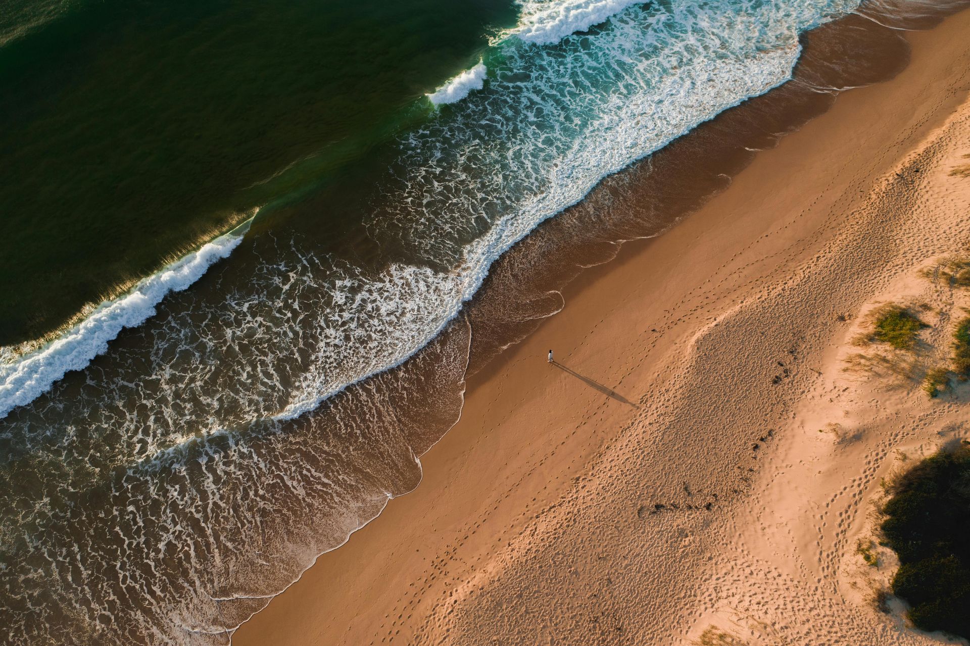 Aerial view of a sandy beach with waves crashing. A person walks along the shore.— GMS Legal & Conveyancing In 38 Canton Beach Rd Toukley, NSW
