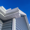 Blue siding and white trim on a building with a gutter against a bright blue sky.