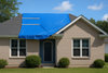 Blue tarp covers a portion of a beige brick house roof, secured with metal bars, on a sunny day.