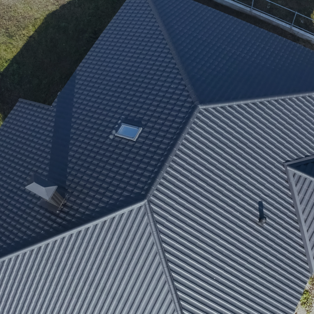 Overhead view of a dark gray house roof with a chimney, skylight, and visible ridges.