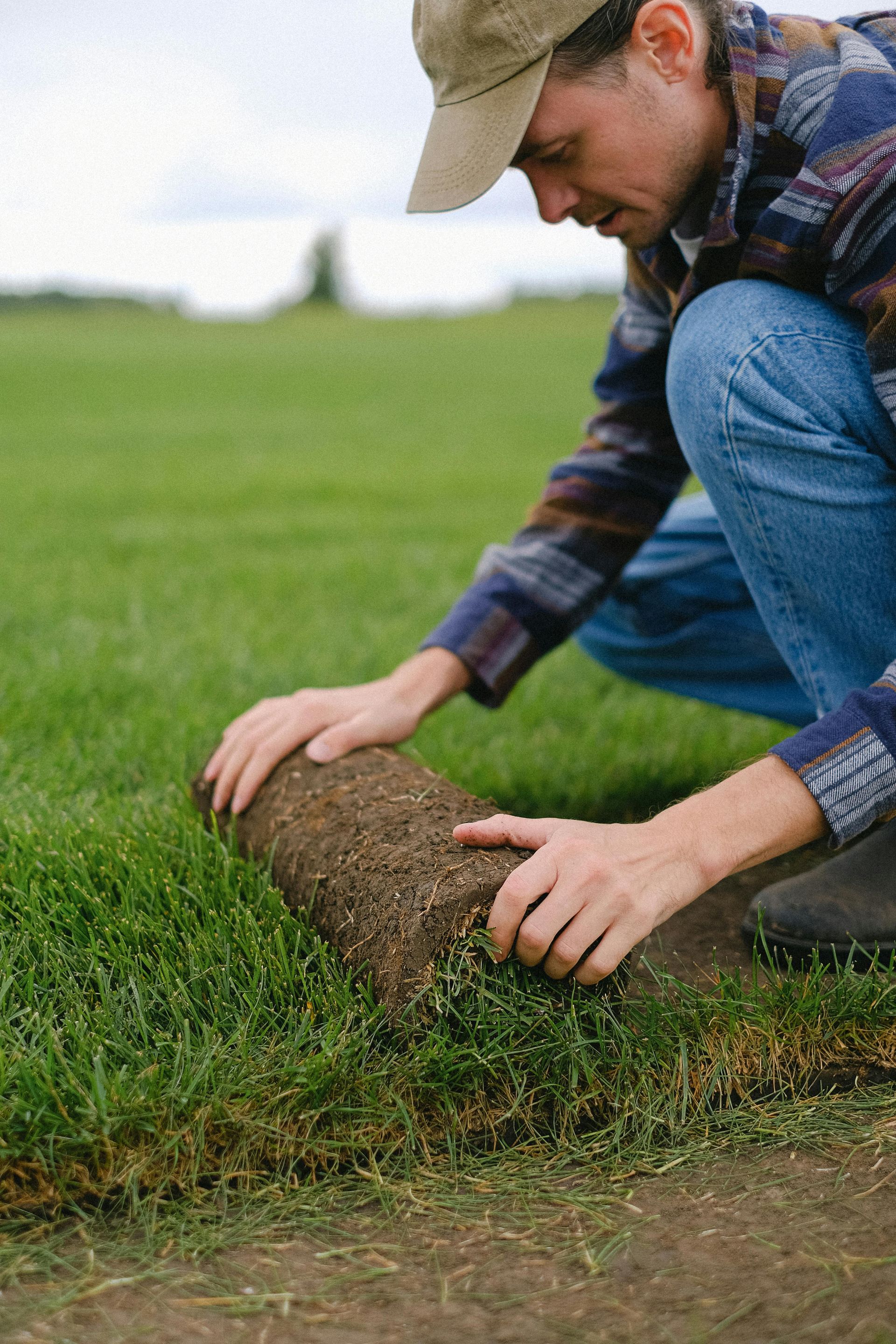 A man is rolling a roll of grass in a field.