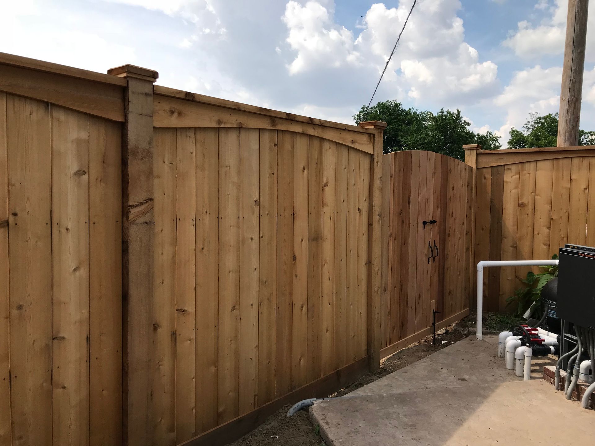 A wooden fence is surrounding a patio with a concrete walkway.