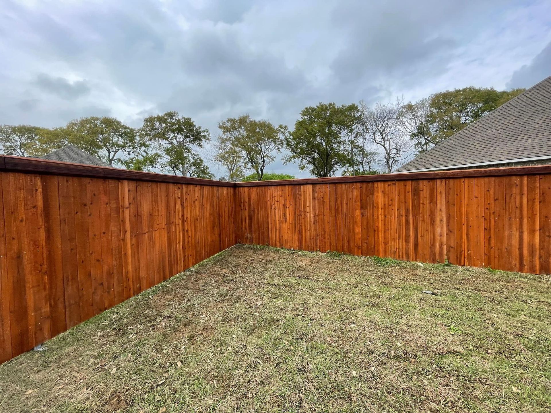 A wooden fence surrounds a lush green yard with trees in the background.