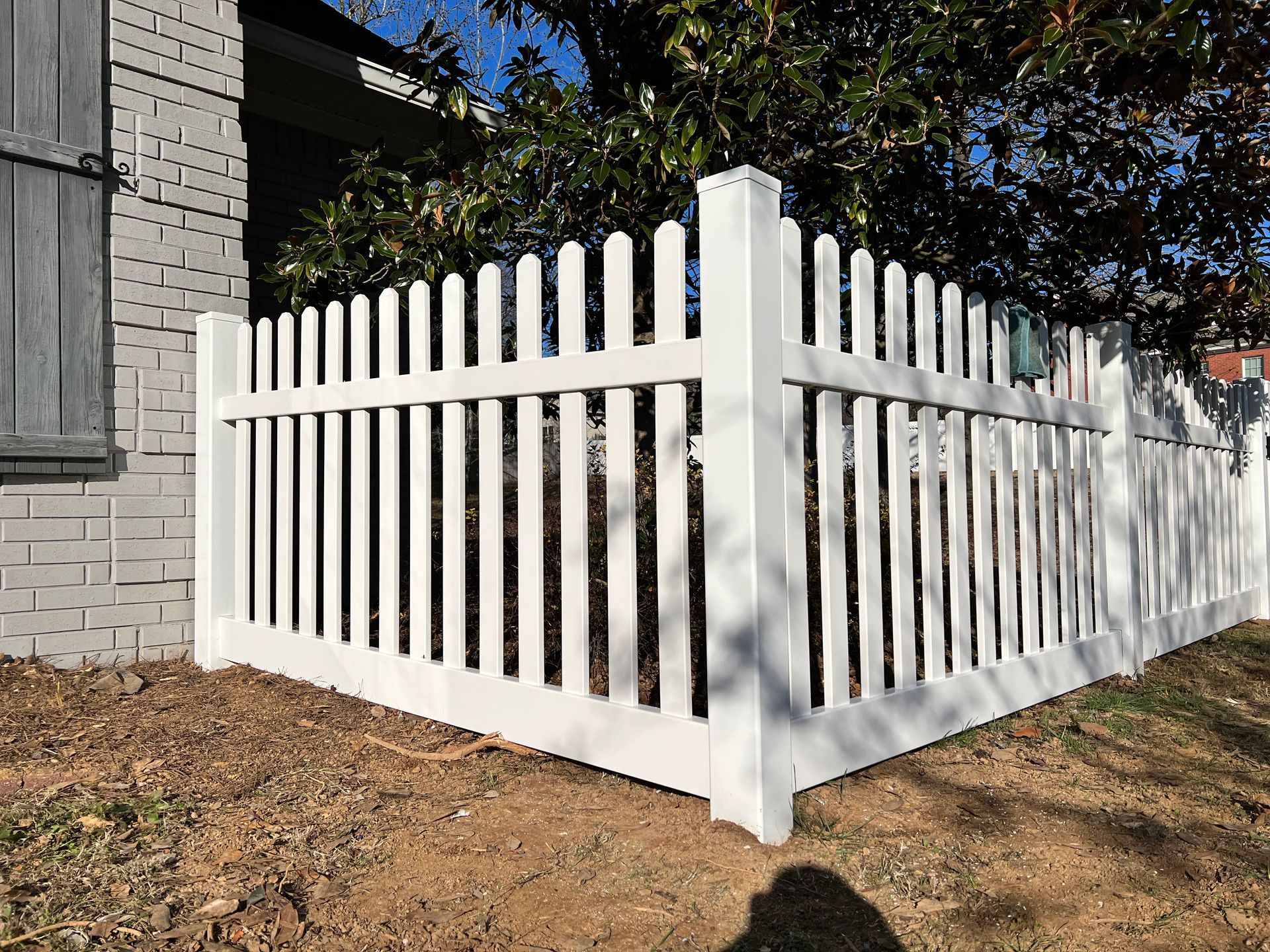 A white picket fence is sitting in front of a brick house.