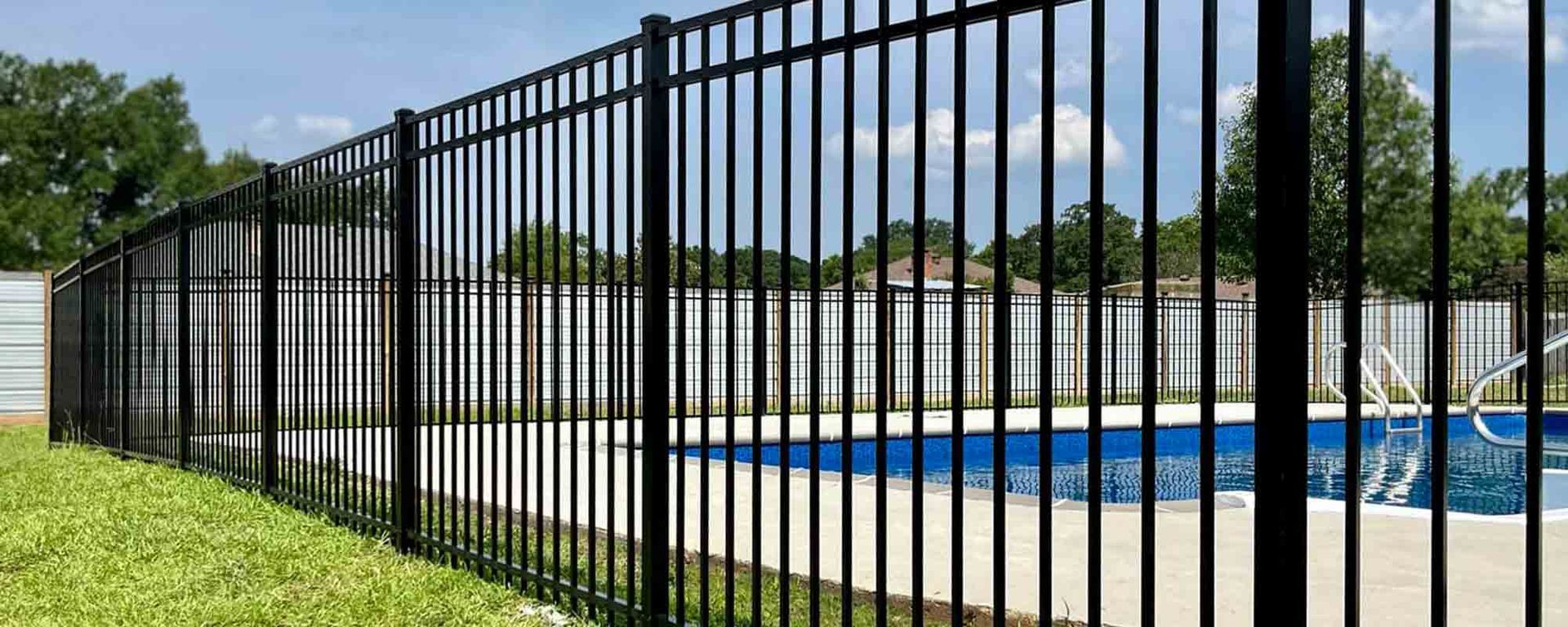 A black metal fence surrounds a swimming pool in a backyard.