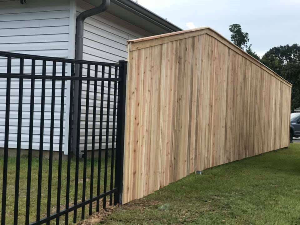 A wooden fence with a black metal fence in front of a house.