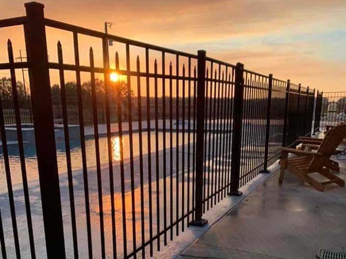 A metal fence surrounds a swimming pool at sunset.