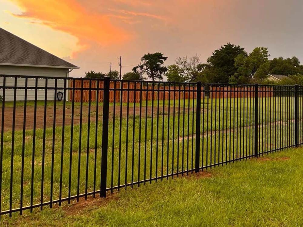 A black metal fence surrounds a grassy field in front of a house.