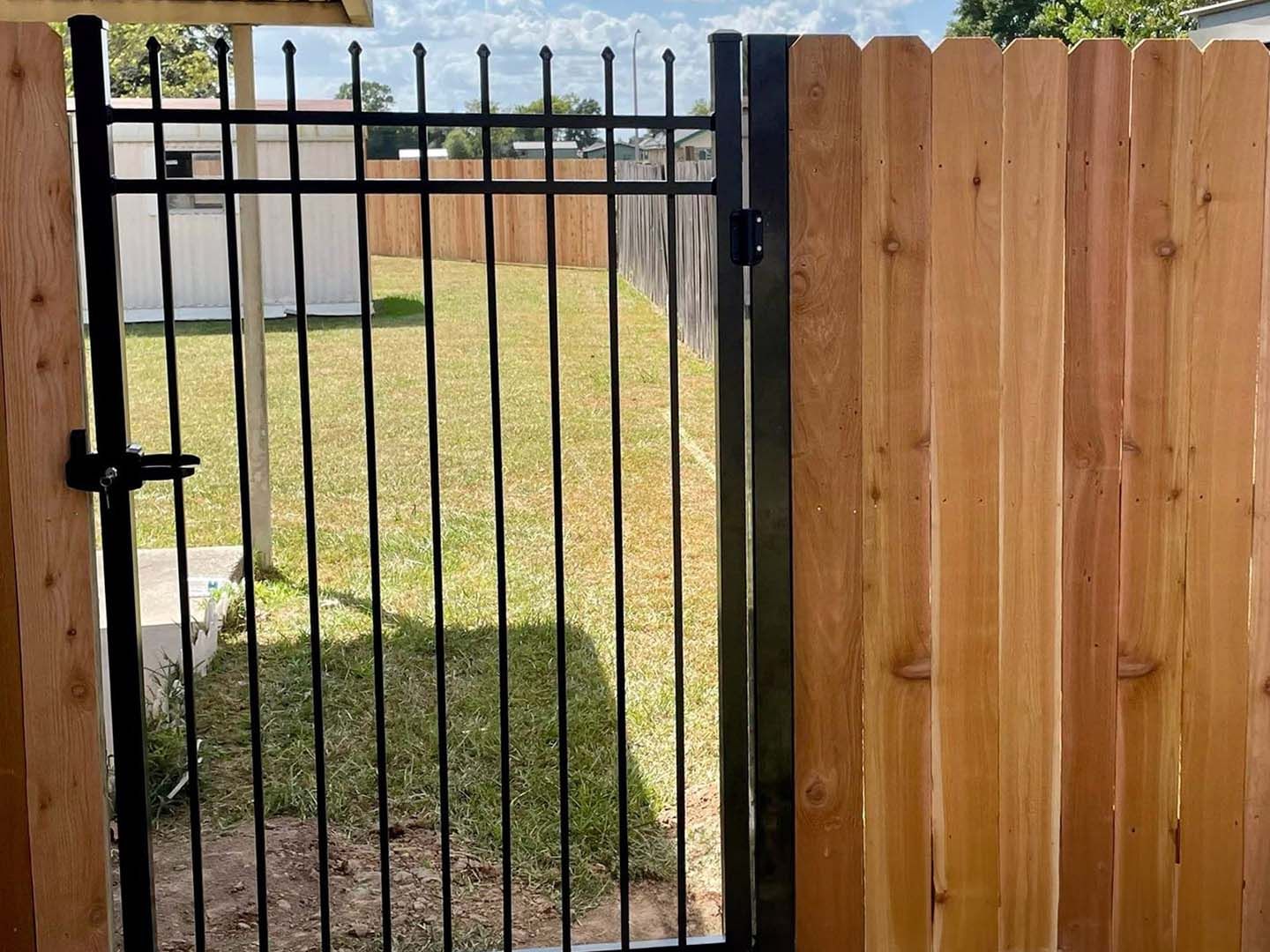 A wooden fence with a metal gate leading to a yard.