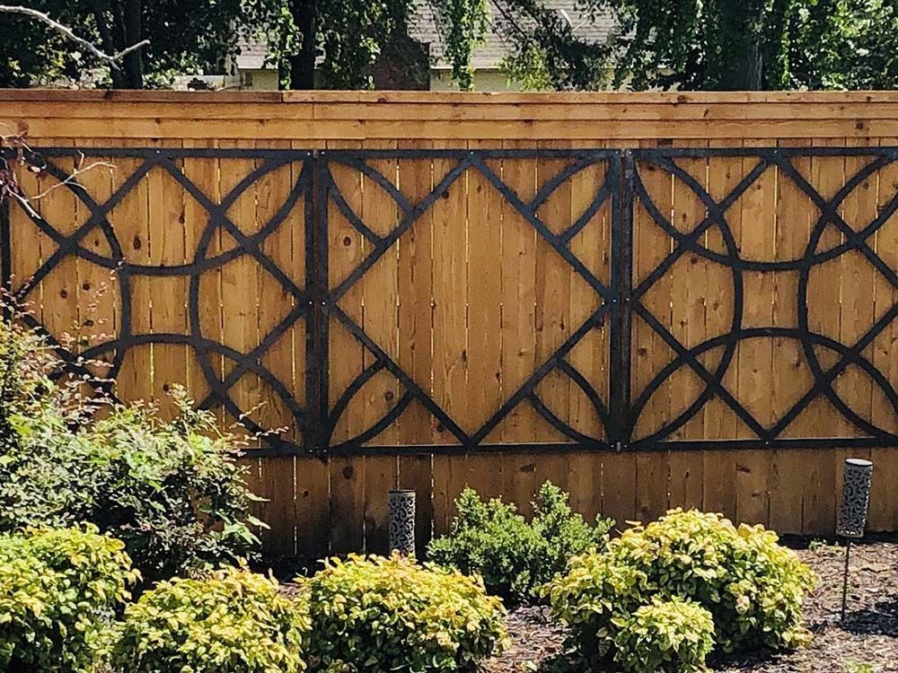 Wooden fence with decorative metal overlay, garden setting with green bushes.