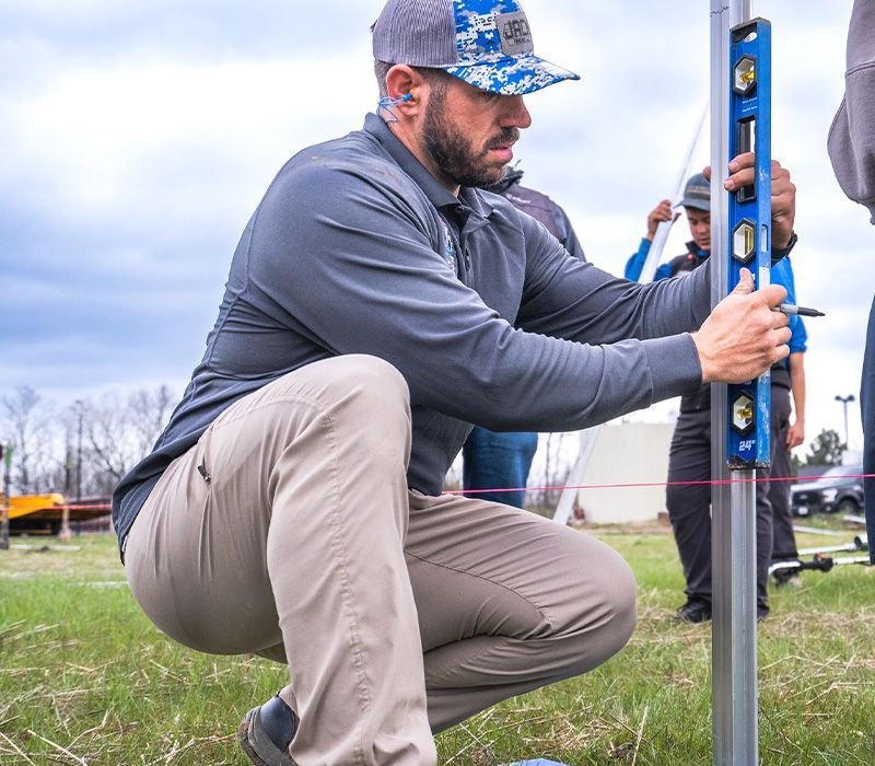 A man squatting down using a blue level on a pole