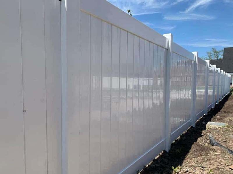 A white vinyl fence is sitting in the dirt next to a house.