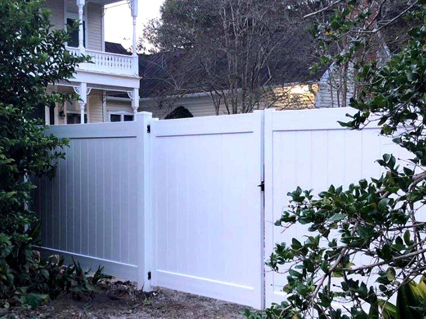 A white fence is surrounded by trees and bushes in front of a house.