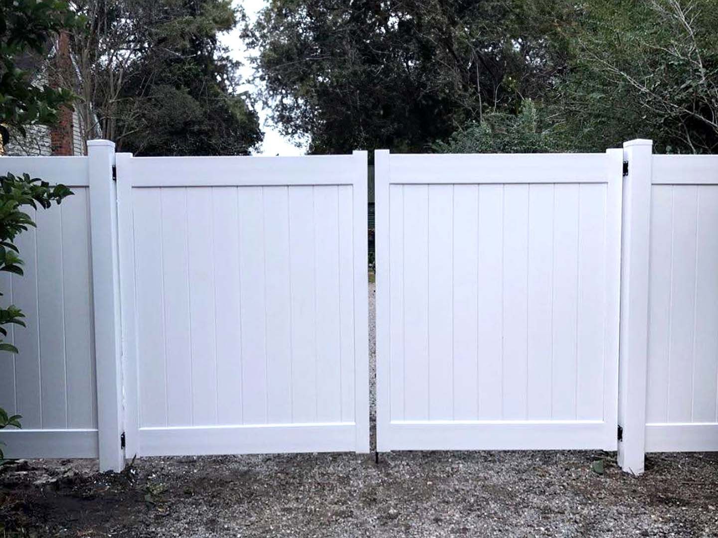 A white fence with a gate in the middle of a gravel driveway.
