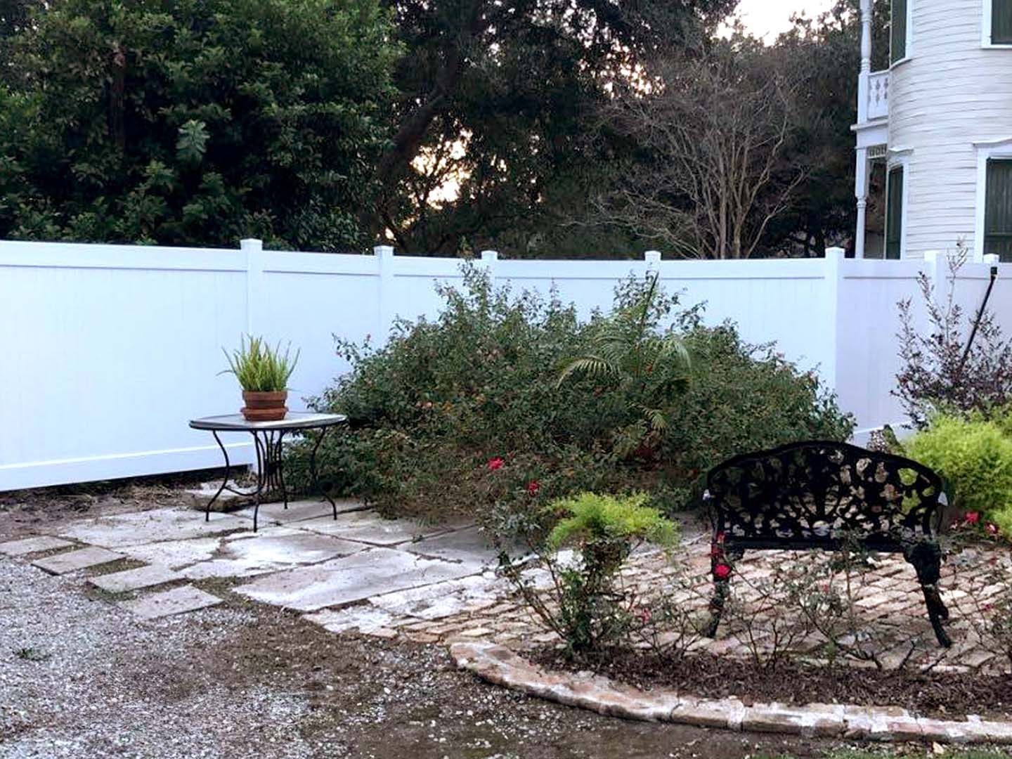 A white fence surrounds a patio with a bench and a table.