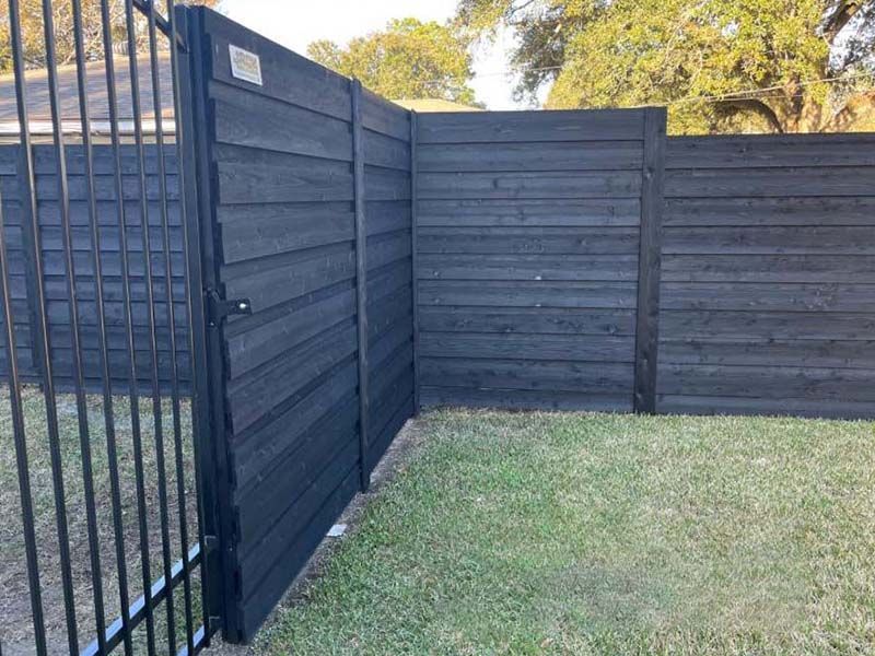 A black wooden fence with a metal gate in a yard.