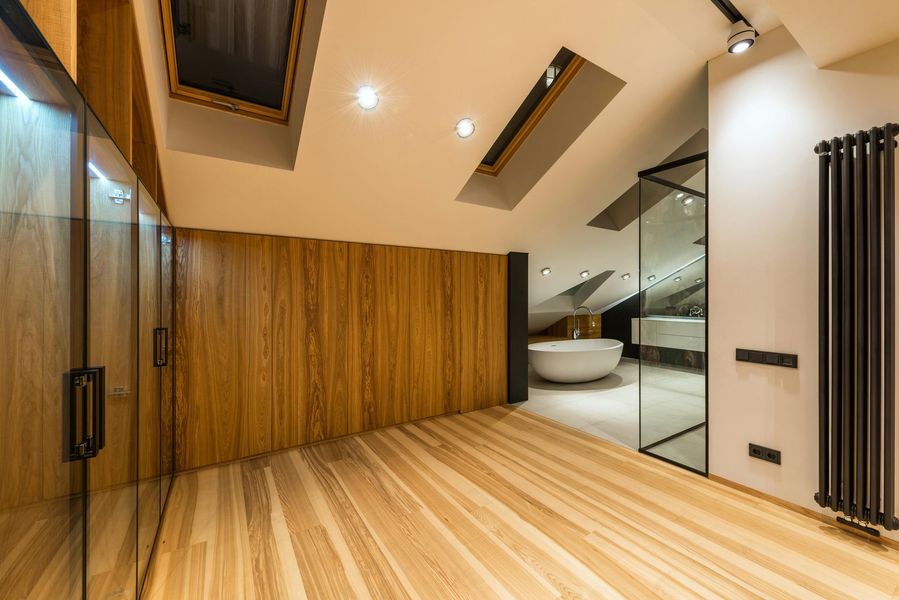 Modern bathroom with wooden walls and floor. A glass shower, white tub, and radiator are visible.