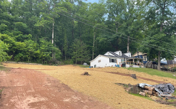 A curved retaining wall made of stacked concrete blocks borders a gravel driveway in front of a house on a grassy hill.