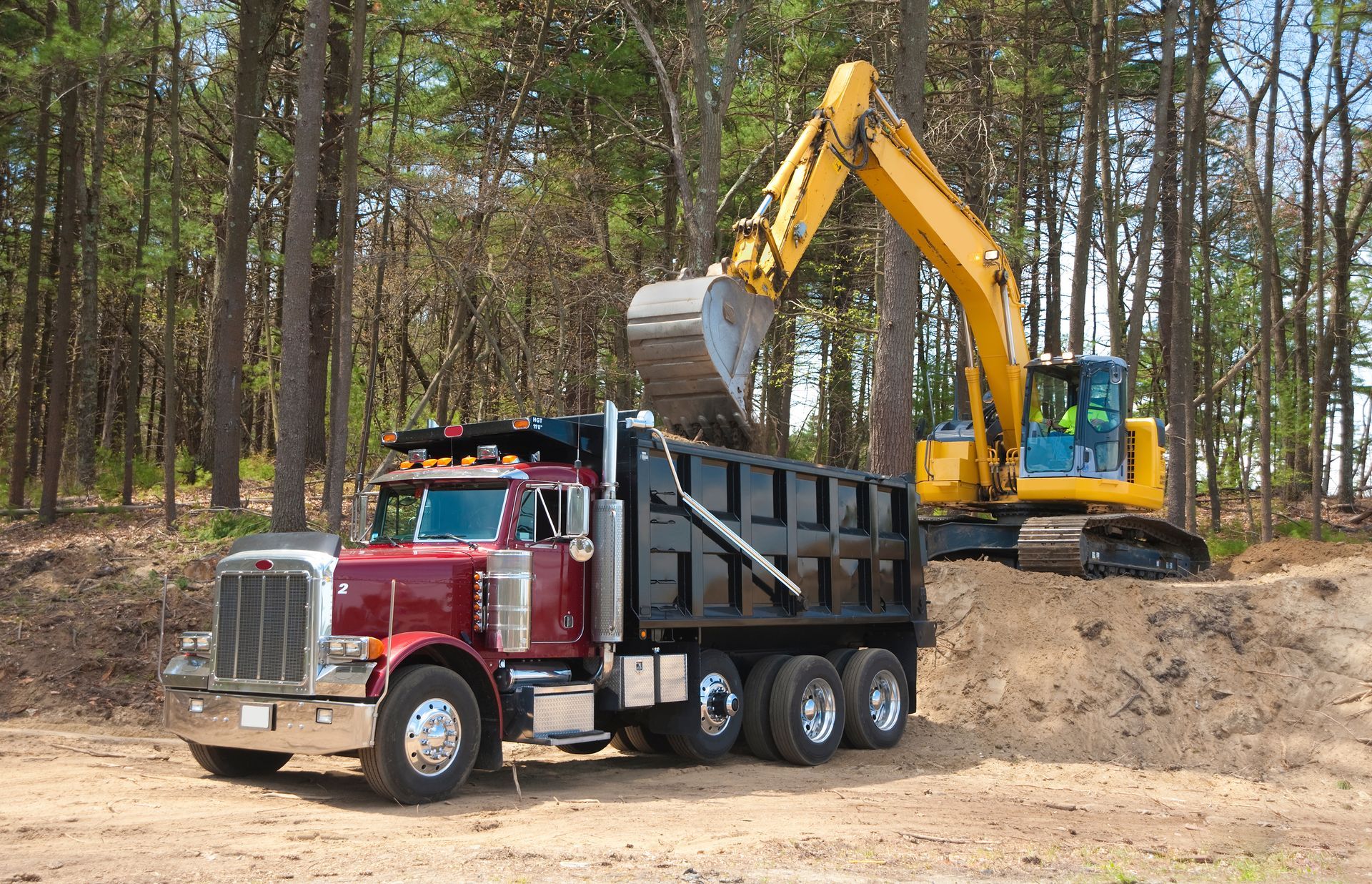 Yellow dump truck filled with wood debris on a gravel road in front of a house.