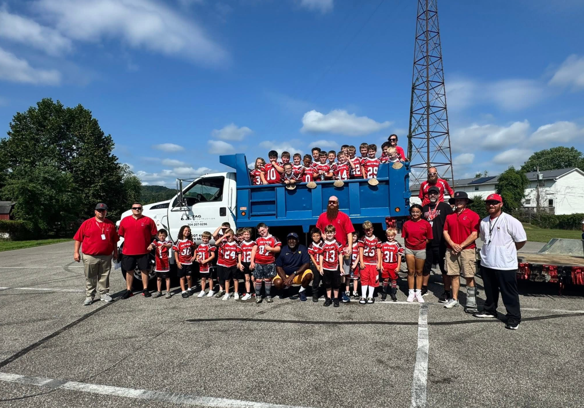 Yellow excavator loading dirt into an orange dump truck at a construction site; worker in vest.