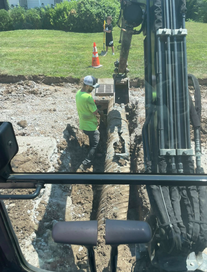 Construction worker reviewing blueprints on-site; other workers stand nearby.