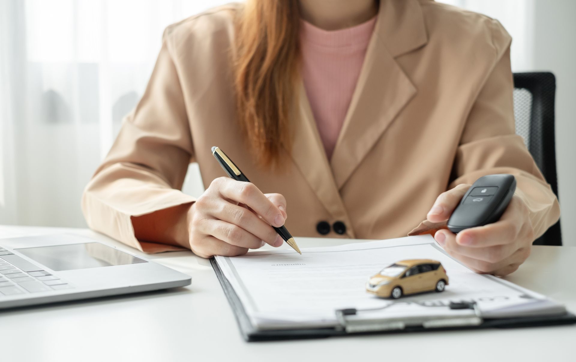 woman is sitting at a desk holding a car key and a pen.