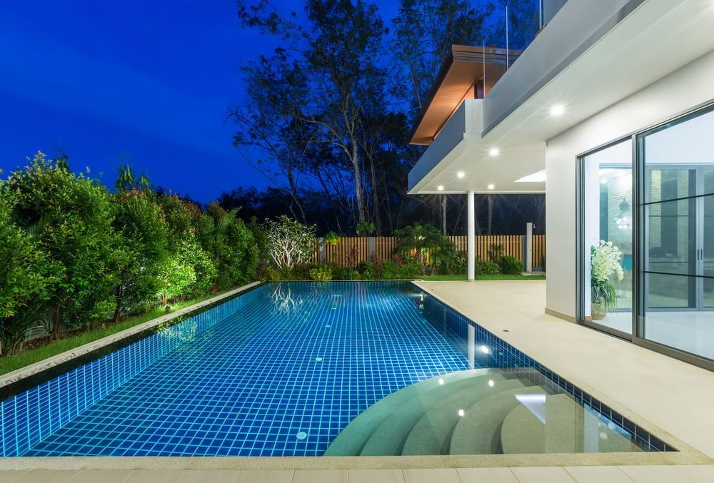 A Large Swimming Pool is in the Backyard of a House at Night — Aqualine Pools in Kalkie, QLD
