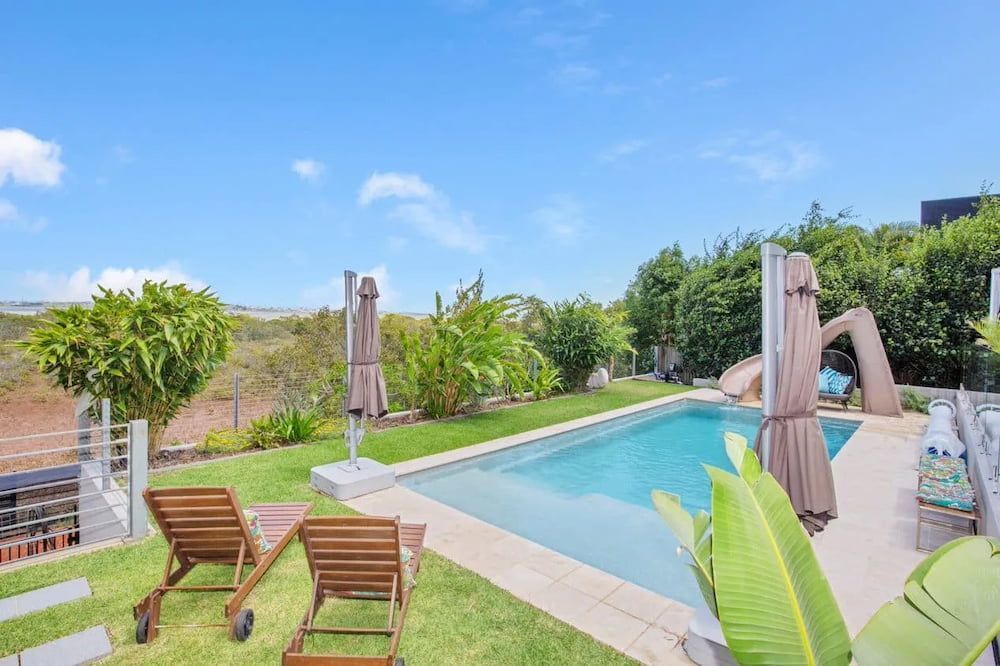A Large Swimming Pool Surrounded by Lawn Chairs and Umbrellas — Aqualine Pools in Burnett Heads, QLD