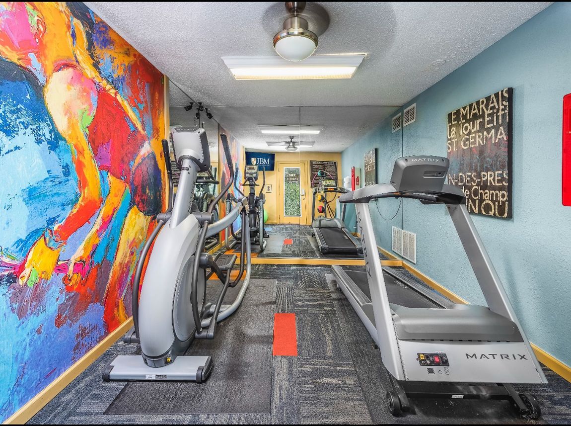 A gym with a treadmill , elliptical , and painting on the wall.