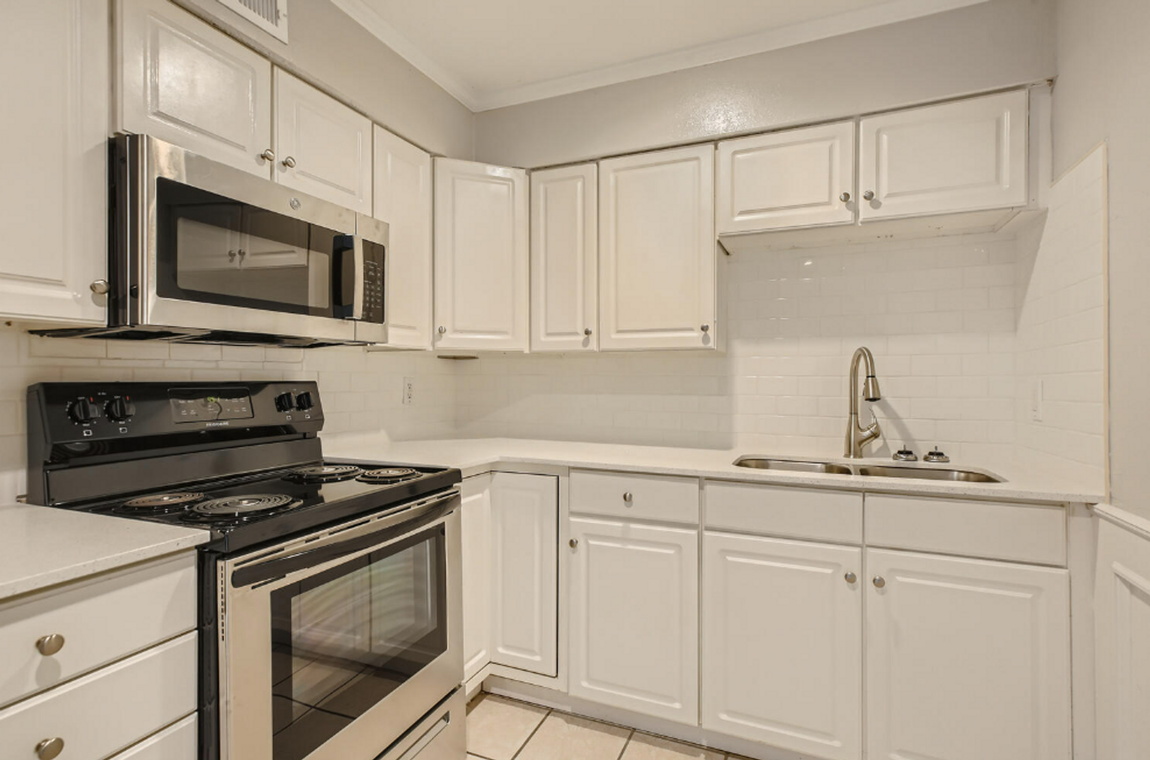 A kitchen with white cabinets , stainless steel appliances , a stove , microwave and sink.