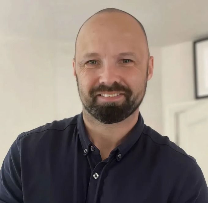 A bald man with a beard wearing a blue shirt is smiling for the camera.