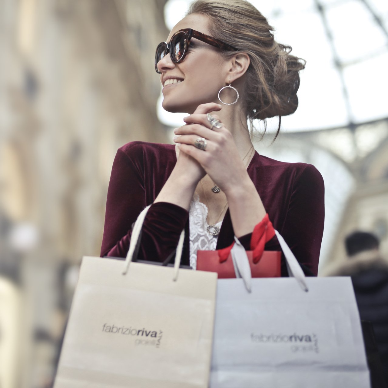 A woman wearing sunglasses is holding two shopping bags with the word rivoli on them