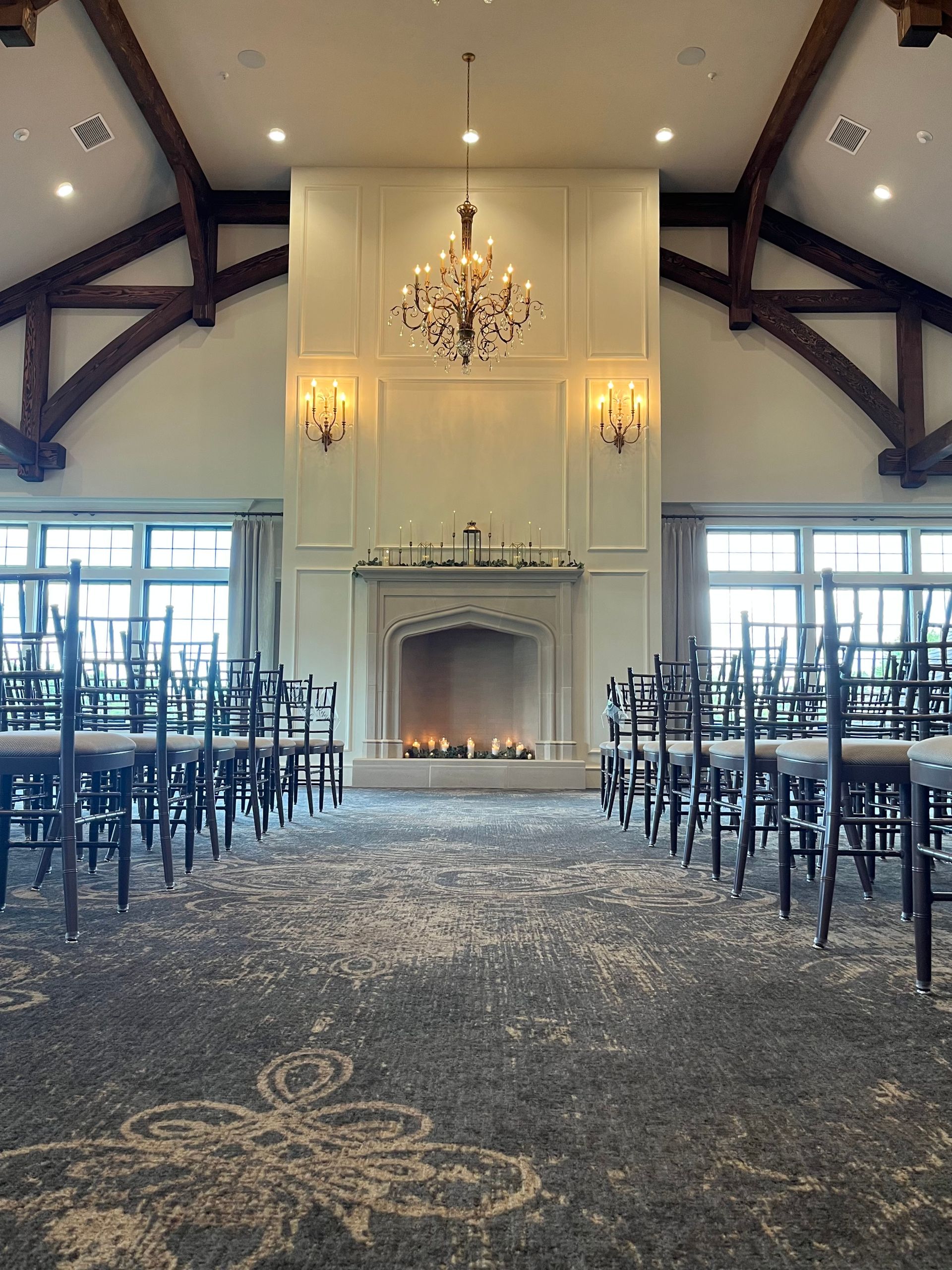Ceremony space with fireplace, chandelier, rows of chairs, and arched wooden beams.