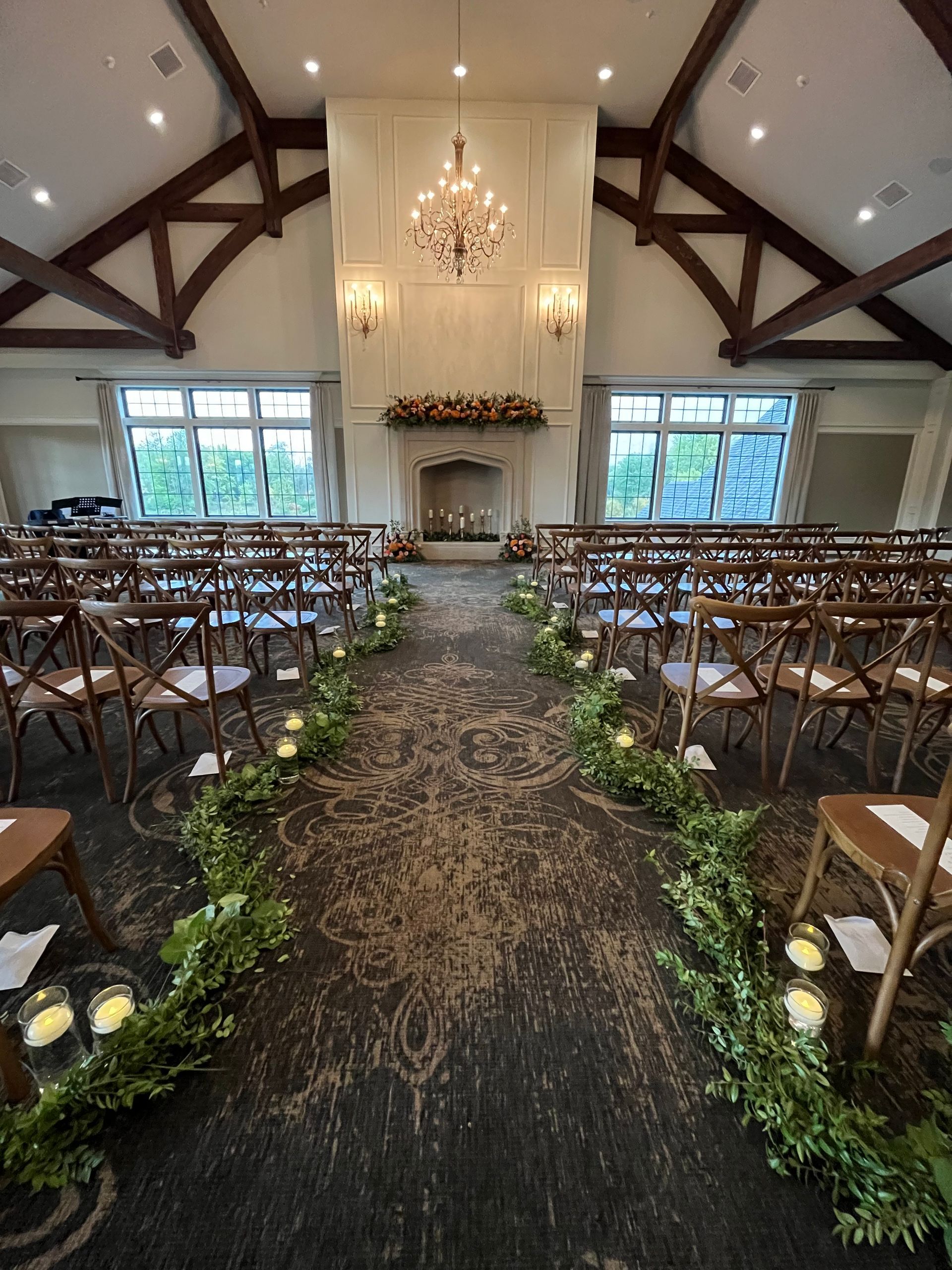 Wedding ceremony setup, indoor venue with floral aisle and wooden chairs.